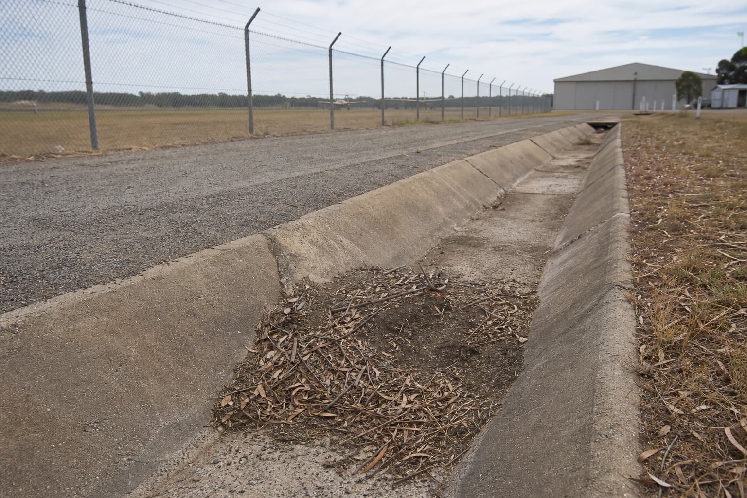 Long open concrete drain beside an airport service area.